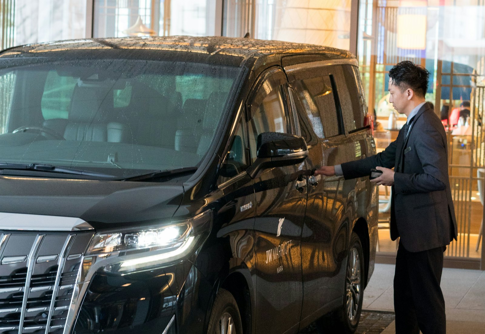 A driver in a suit opening the passenger door of a black transfer van